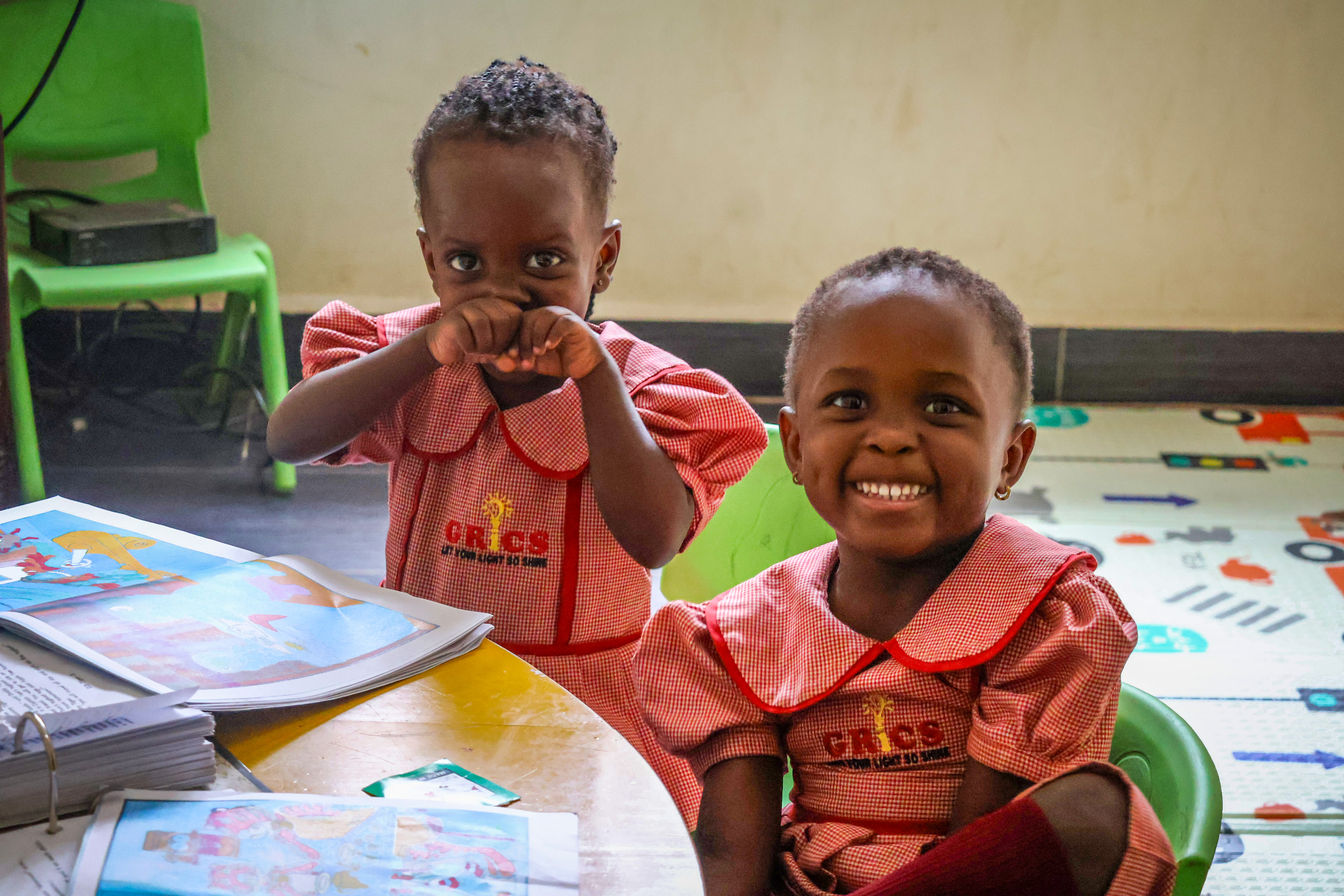 Two young GRICS learners smiling together at their desk